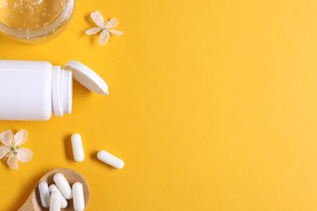 Collagen capsules, gel and flowers on orange background, flat lay. Space for text