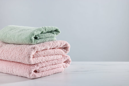 Stack of clean towels on white marble table against light background, space for textの写真素材