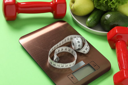Electronic kitchen scale, measuring tape, dumbbells and products on light green background, closeup....
