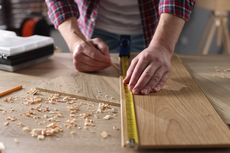 Man measuring wooden plank with tape indoors, closeupの写真素材