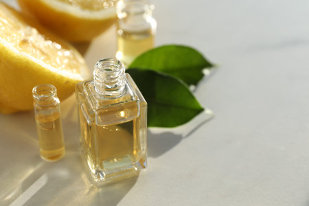 Perfume bottles with aromatic oils and lemons on light background, closeup. Space for text