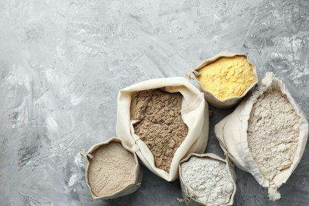 Different types of flour in bags on grey textured table, flat lay. Space for textの写真素材