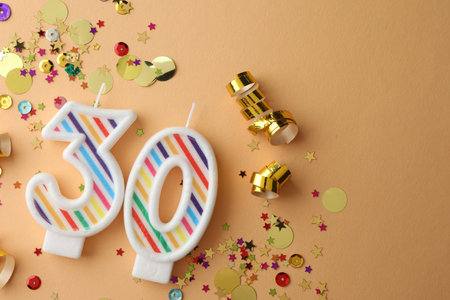 30th birthday. Number shaped candles and confetti on beige background, flat lay. Space for text