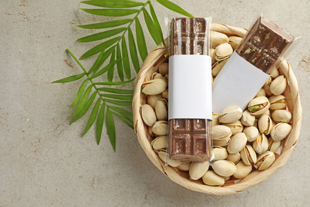 Delicious chocolate bars, pistachios and leaves on light background, top view