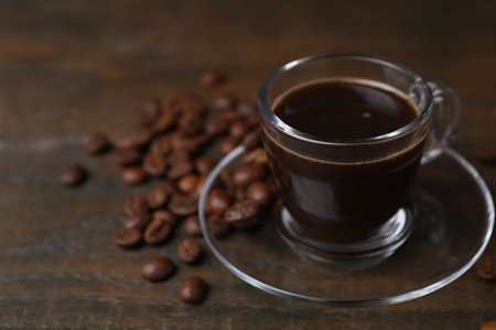 Aromatic coffee in glass cup and beans on wooden table, closeup. Space for textの写真素材
