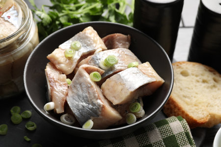 Pieces of herring with green onions on black table, closeupの写真素材
