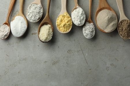 Different types of flour in spoons on light grey table, flat lay. Space for textの写真素材