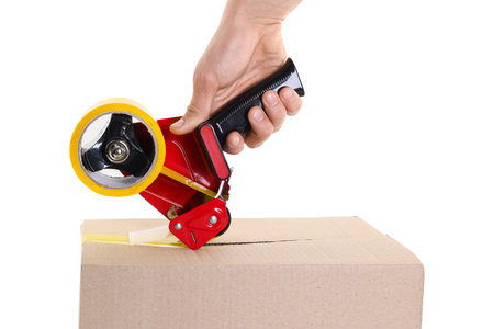Man using dispenser with adhesive tape to seal cardboard box on white background, closeup
