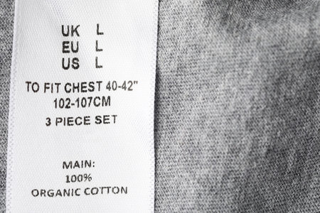 Clothing label with size and content information on grey garment, above view. Space for textの写真素材