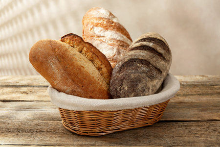 Different loaves of fresh bread in basket on wooden table, closeup