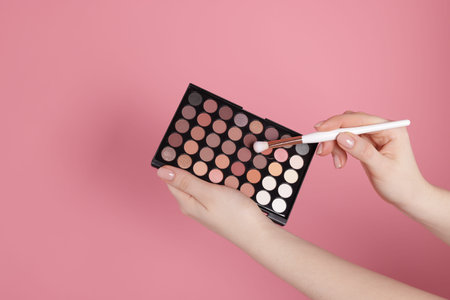 Woman with eyeshadow palette and brush on pink background, closeupの写真素材