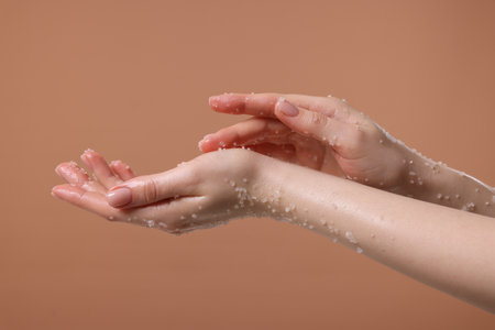 Woman applying body scrub onto her hand against dark beige background, closeupの写真素材