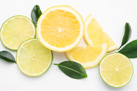 Slices of fresh lemons, limes and leaves on white background, flat layの写真素材