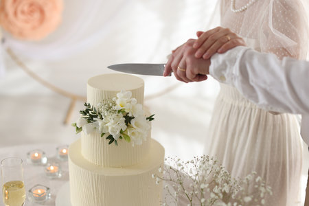 Married couple cutting delicious wedding cake with knife at table indoors, closeupの写真素材
