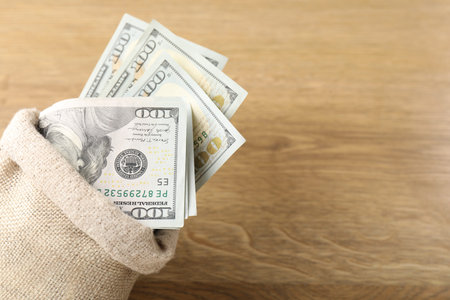 Bag with many dollar banknotes on wooden table, closeup. Space for text