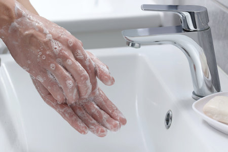 Woman washing her hands with foaming soap above sink in bathroom, closeup
