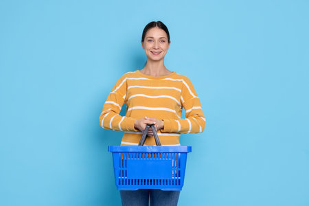 Smiling woman with shopping basket on light blue backgroundの写真素材