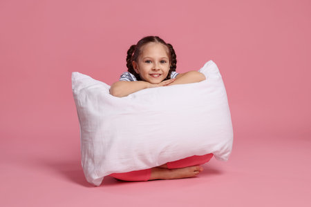 Cute girl with pillow on pink backgroundの写真素材