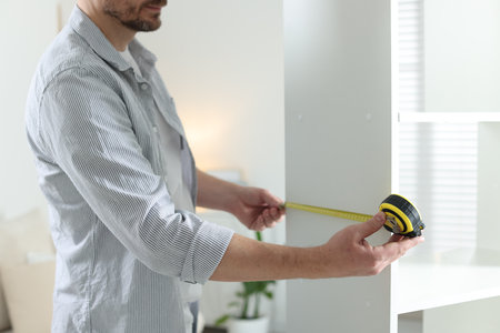 Man measuring white shelving unit with tape indoors, closeupの写真素材