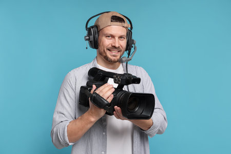 Man with professional video camera and headset on light blue backgroundの写真素材