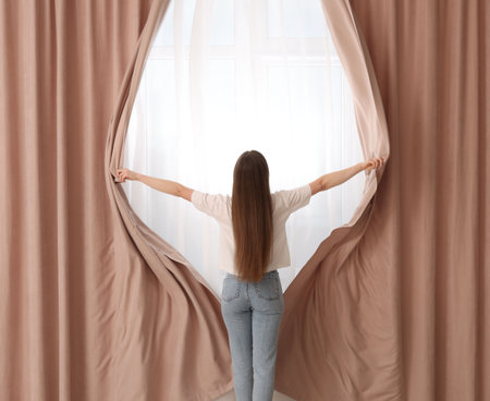 Woman opening stylish curtains at home, back viewの写真素材