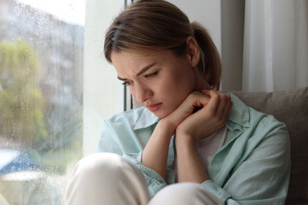 Depressed woman sitting near window at homeの写真素材