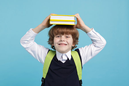 Cute schoolboy with backpack and books on light blue background