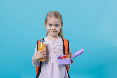 Cute little girl with lunch box and drink on light blue backgroundの写真素材