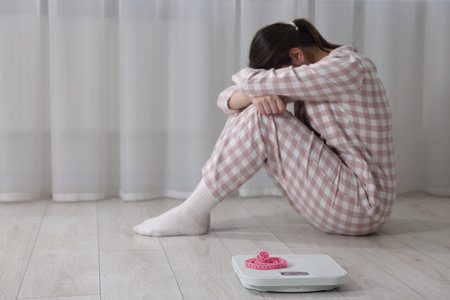 Depressed woman, scales and measuring tape on floor at home, selective focus with space for text.の写真素材
