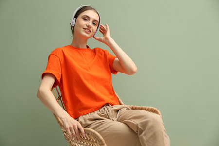 Beautiful woman with headphones relaxing in comfortable wicker armchair near pale green wall indoors