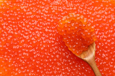 Delicious red caviar and spoon as background, top view. Space for text