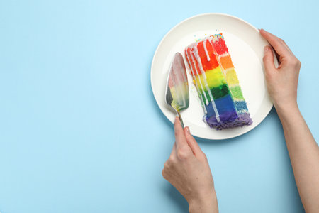 Woman with piece of delicious rainbow cake and spatula at light blue table, top view. Space for textの写真素材