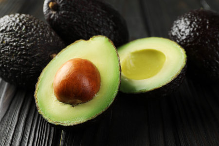 Whole and cut avocados on dark wooden table, closeup