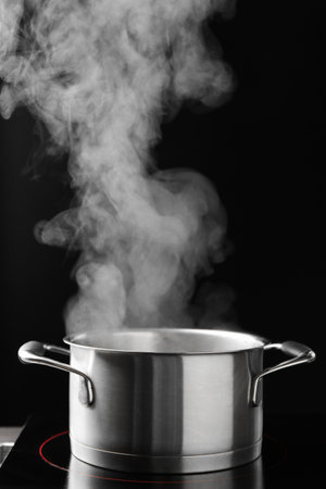 Steam rising from cooking pot and stove on black background, closeupの写真素材