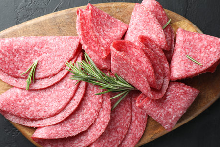 Slices of delicious sausage with rosemary served on black table, top view