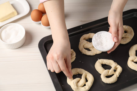 Woman putting salt onto raw pretzels at white wooden table, closeup