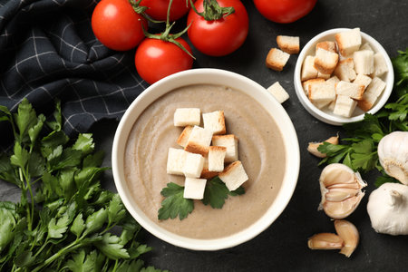Delicious mushroom cream soup with croutons, parsley and ingredients on black table, flat layの写真素材