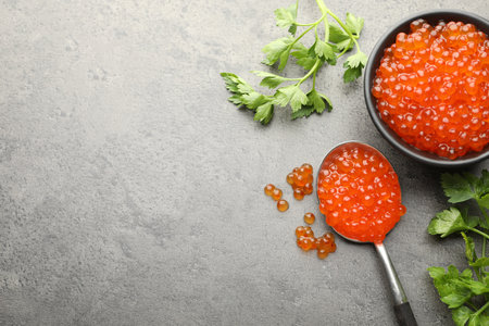 Tasty red caviar in bowl, spoon and parsley on grey table, flat lay. Space for textの写真素材