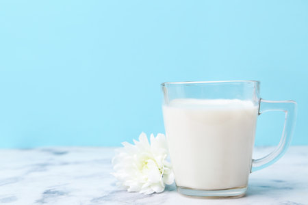 Cup of milk and flower on white marble table against light blue background. Space for textの写真素材