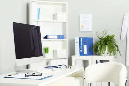 Doctor's workplace. Computer monitor, clipboard, stethoscope and glasses on white table in medical officeの写真素材