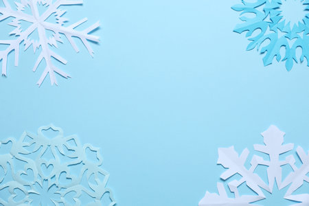 Beautiful paper snowflakes on light blue background, flat lay. Space for textの写真素材