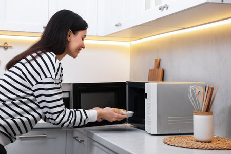 Woman putting plate with lunch into microwave indoorsの写真素材
