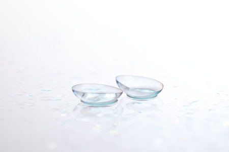 Pair of contact lenses and water drops on white mirror surface, closeupの写真素材