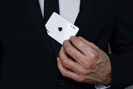 Illusionist hiding playing card behind jacket lapel on gray background, closeup
