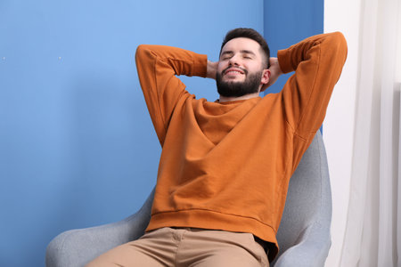 Smiling man relaxing on armchair at homeの写真素材