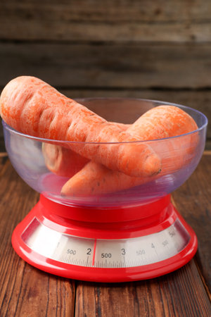 Kitchen scale with fresh carrots on wooden table, closeupの写真素材