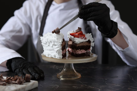 Confectioner decorating pieces of tasty cake at black marble table in kitchen, closeupの写真素材