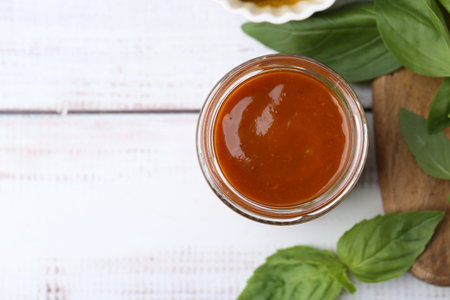 Tasty curry sauce in glass jar and basil on white wooden table, flat lay. Space for textの写真素材