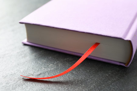 Book with red ribbon bookmark on dark textured table, closeup