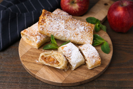 Tasty apple strudels with powdered sugar, mint and fruits on wooden table, closeupの写真素材